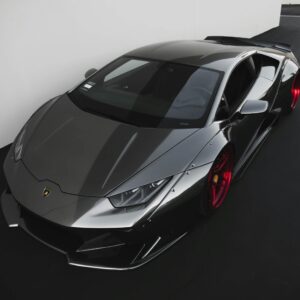 Sleek metallic Lamborghini sports car with vibrant red wheels parked indoors.